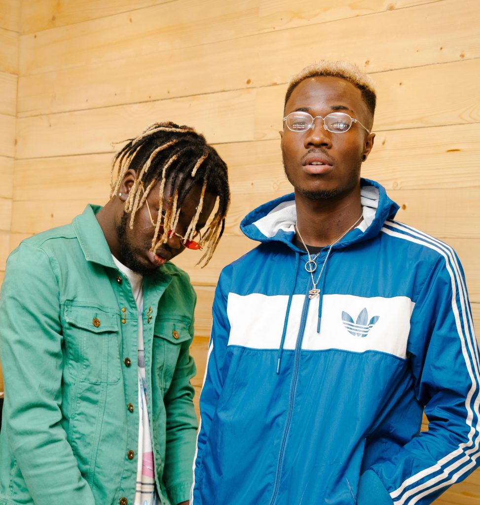 Two Standing Men Posing Beside Wooden Wall